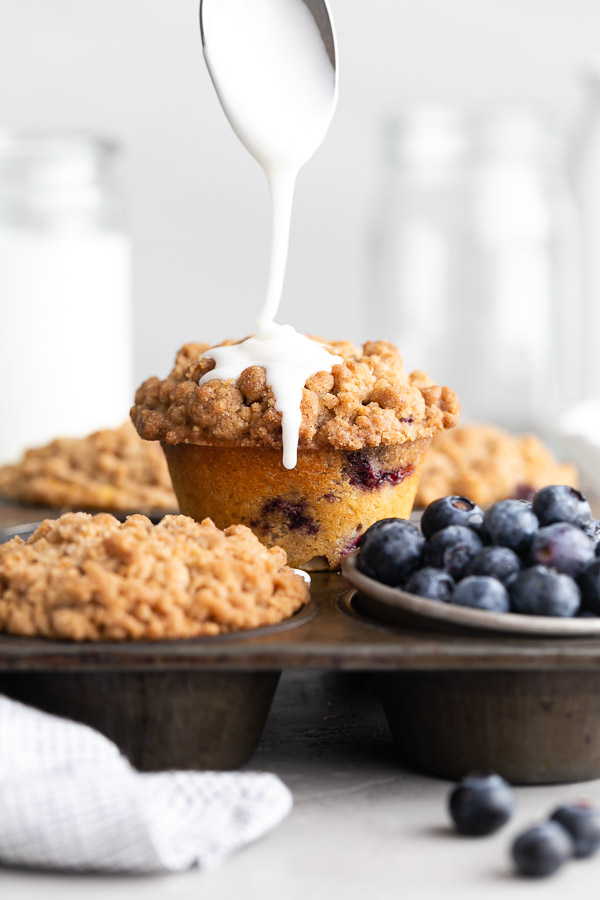 drizzling vanilla glaze on top of blueberry streusel muffin